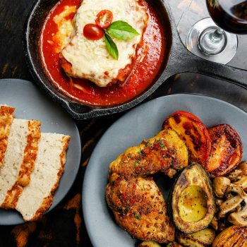 Top-down view of Chicken Parmesan with grilled vegetables and wine, a classic Italian dinner setting.